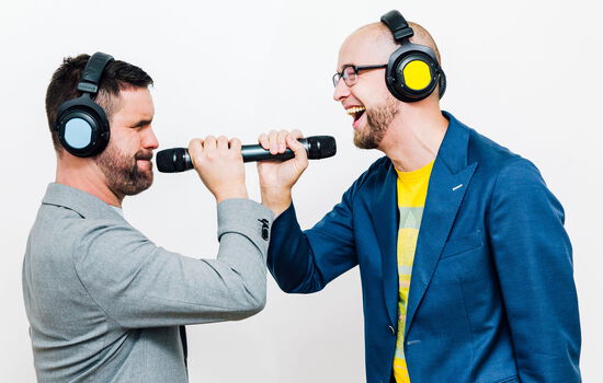 Oliver und Lukas stehen sich mit Mikros und Kopfhörern gegenüber